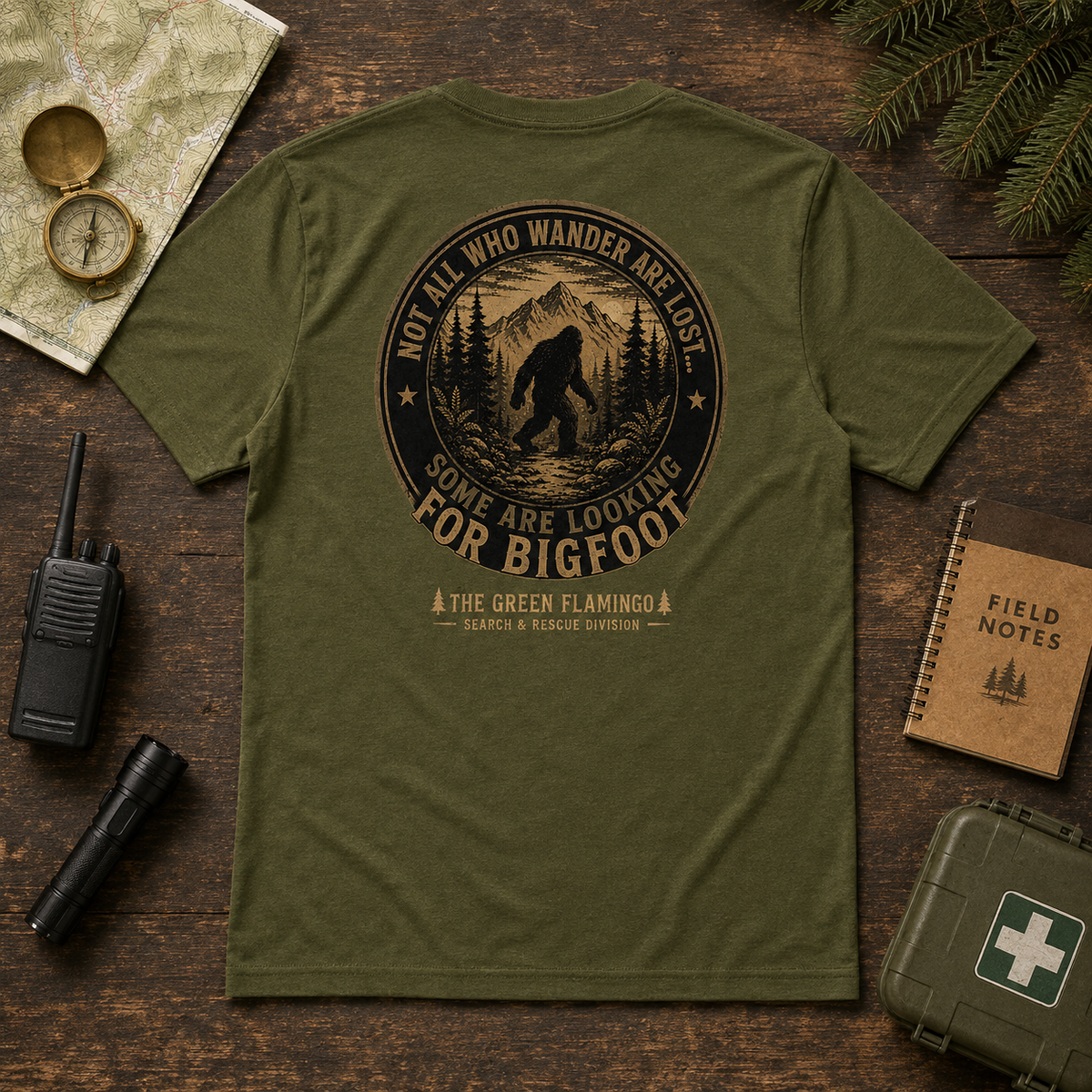 Olive Looking for Bigfoot Search and Rescue T-shirt back graphic in an outdoor adventure flat lay